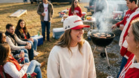 Group of people at a casual outdoor gathering with a woman wearing a red and white cap.